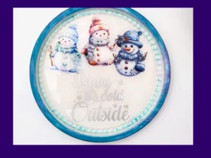 Round AquaCast resin snowman tray with three illustrated snowmen and “Baby it’s cold outside” text.