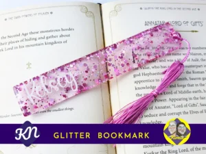 Pink heart-shaped glitter bookmark personalised with the name Kelsey, displayed on an open book with a matching pink tassel.