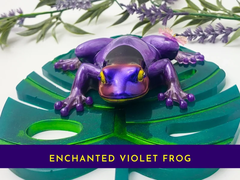 “Purple resin frog with a butterfly on its back on a green leaf base, with a purple banner reading ‘Purple Frog’.”