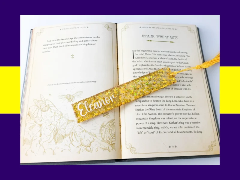 Yellow glitter bookmark personalised with the name Eleanor, resting diagonally across an open book with a matching gold tassel.