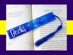Blue glitter bookmark personalised with the name Becki, displayed on an open book with a matching blue tassel.