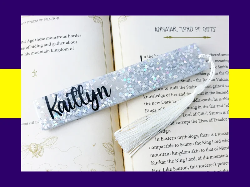 White Silver star glitter bookmark personalised with the name Kaitlyn, resting on an open book with a white tassel.