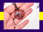 Round resin pendant in pink, burgundy and black with copper wire wrap shown in hand – handmade autumn inspired necklace