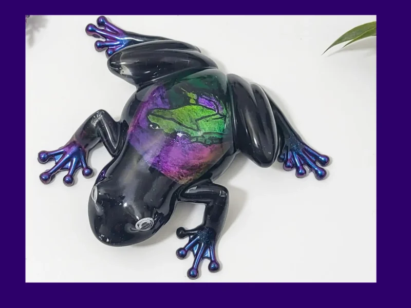 Enchanted Prism Frog resin ornament shown from above, with purple lettering on a banner across the image.