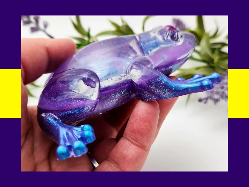 Hand holding the Aqua Purple Frog resin figurine, showing the shimmer, blue toes, and translucent purple body