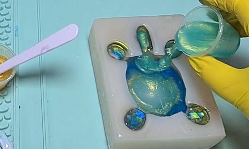 Close-up of hands creating resin art with pigments and tools in the Kirnix craft studio.