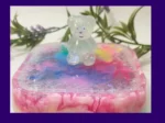 Close-up of a clear glitter teddy sitting on the lid of a pastel rainbow resin treasure box with iridescent sparkle flakes.