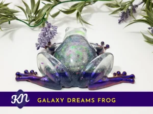 Rear view of the glittery resin frog showing the rounded back and outstretched purple legs; branded banner reads “GALAXY DREAMS FROG”.
