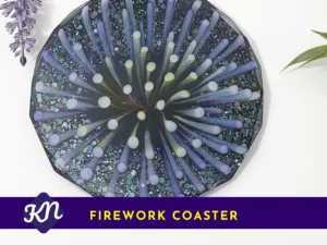 Top-down photo of a dark blue and lilac “firework burst” resin coaster with scattered glitter; a purple banner at the bottom shows a KN logo and the words “FIREWORK COASTER”.