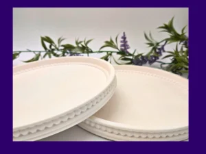 wo white Pearl Rim Round Trays photographed at an angle, showing the beaded edge detail with faux greenery behind.