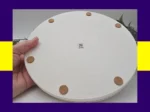 Underside of the Pearl Rim Round Tray showing cork feet and a small QR label, held in hand, with purple and yellow border.