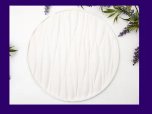 White round tray with raised wave texture photographed flat lay with greenery and lavender around the edges, framed by a purple border.