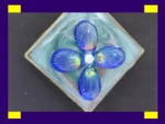 Close-up of a square resin pendant with iridescent blue petal design inside a metal frame.