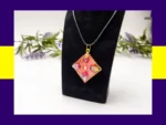 Red-toned square resin petal pendant necklace displayed on a black jewellery stand.
