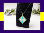 Teal-and-cream square resin petal pendant necklace displayed on a black jewellery stand.