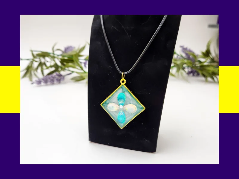 Teal-and-cream square resin petal pendant necklace displayed on a black jewellery stand.
