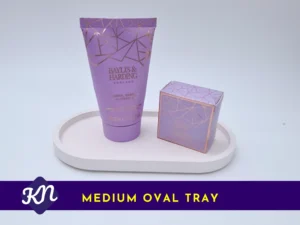 Medium oval Aquacast eco resin trinket tray in soft white, shown holding toiletries; “Medium Oval Tray” label on a Kirnix purple/yellow banner.