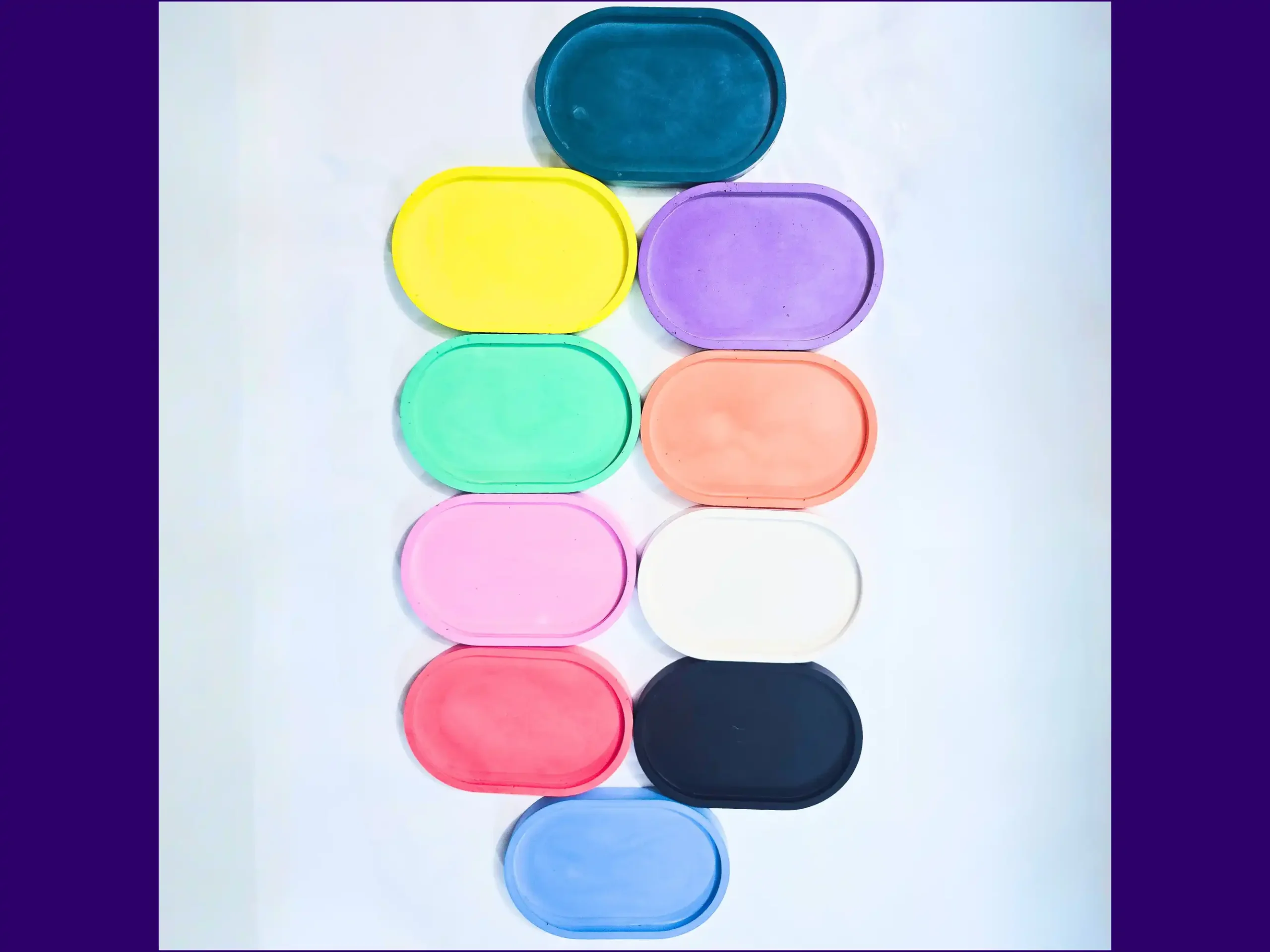 Stacked colour selection of small oval eco resin trays arranged vertically on white background.
